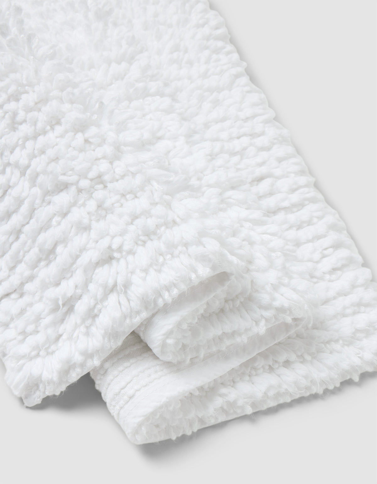 A close-up of the Cozy Earth Plush Loop Bath Mat, folded on a light gray background. The mat’s fluffy, looped texture highlights its softness and absorbency.