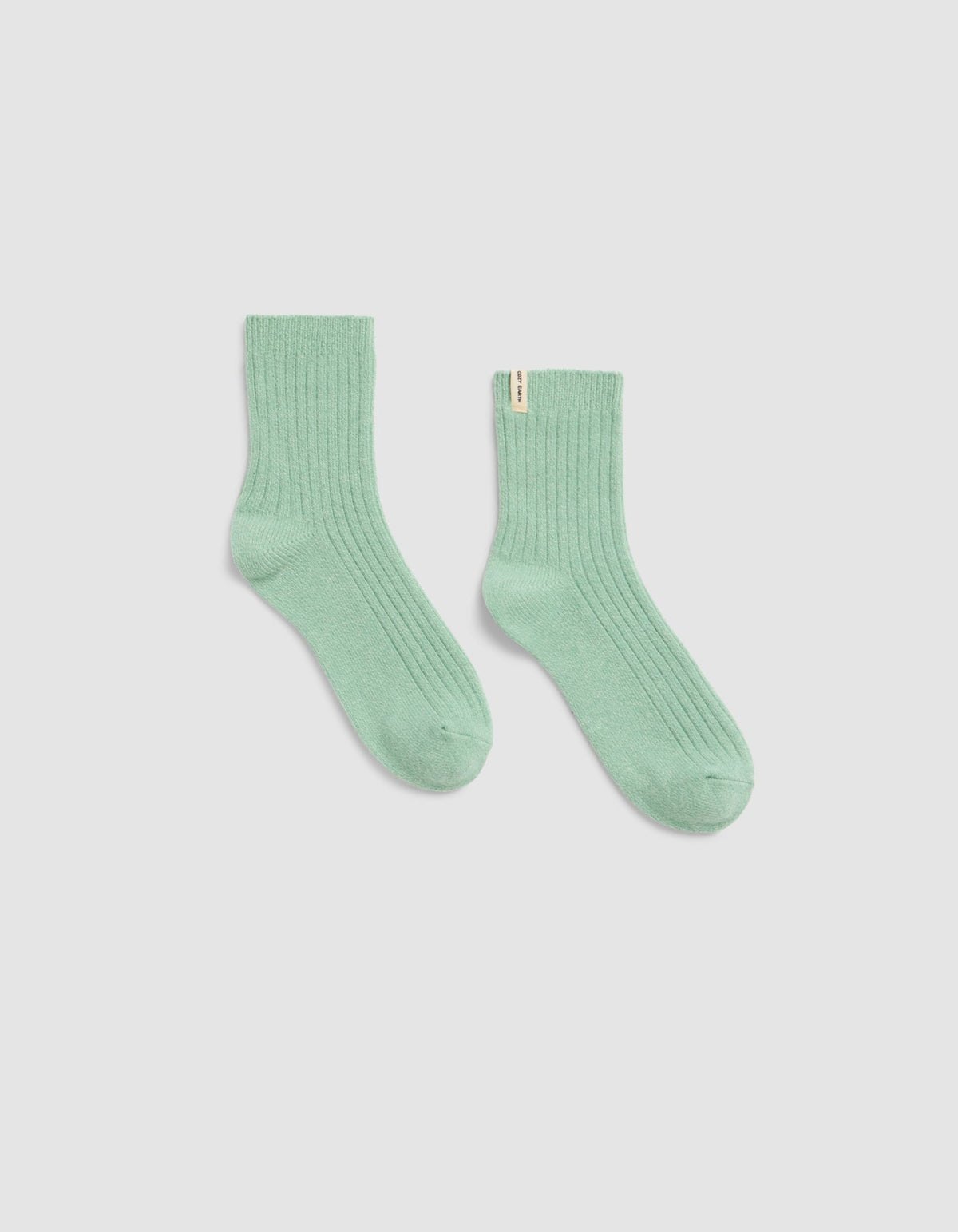 A pair of Plush Lounge Quarter Sock by Cozy Earth, in light green ribbed fabric, is laid flat on a plain white background with one sock slightly angled outward.