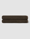 Two dark brown towels from the Cozy Earth Complete Ribbed Terry Bath Bundle are neatly rolled and stacked atop each other against a plain light gray background.|Color:Espresso