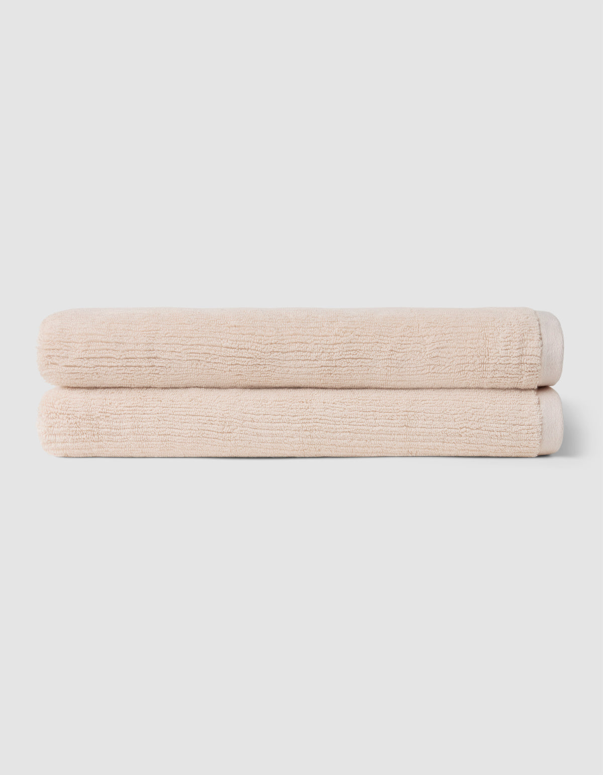 Two neatly folded beige towels from Cozy Earth's Complete Ribbed Terry Bath Bundle are stacked on top of each other against a plain light gray background.|Color:Petal
