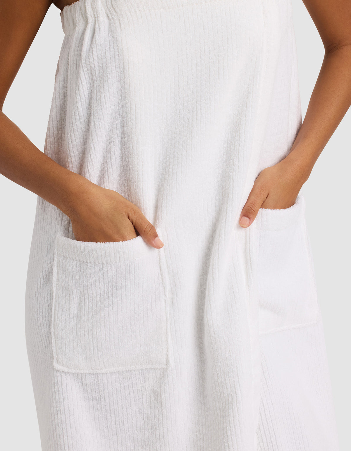 A person wears the Cozy Earth Ribbed Terry Bath Wrap, hands tucked into its large front pockets. Only their torso and hands are visible against a plain light background.