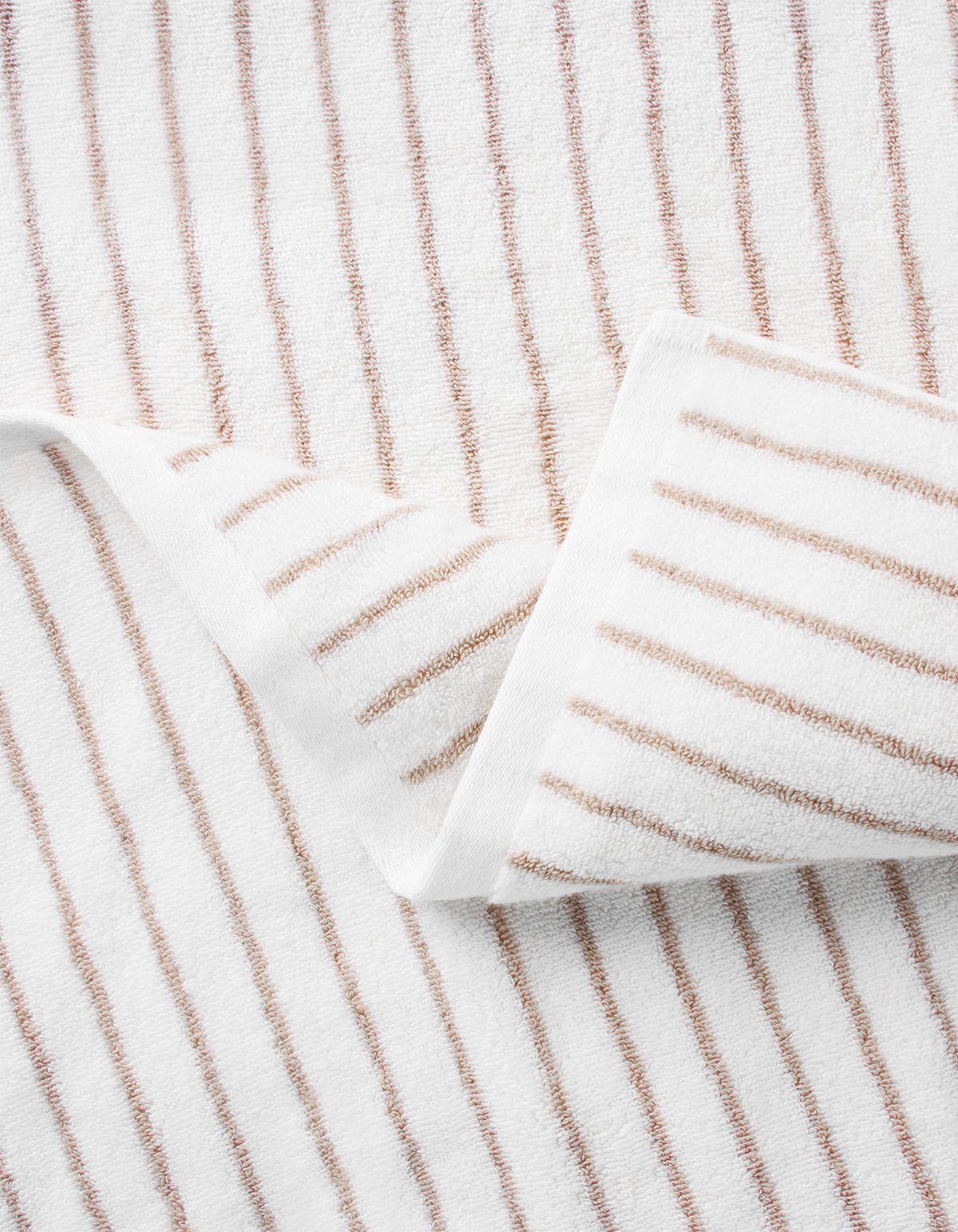 A close-up of the Cozy Earth Complete Striped Luxe Bath Bundle, featuring a partially folded white towel with evenly spaced thin brown stripes showing the elegant pattern on both sides. 