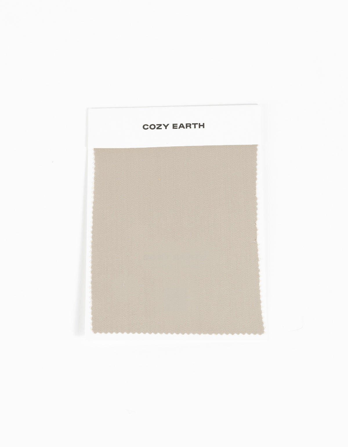 A rectangular beige Soft-Wash Cotton Sheet Swatch from Cozy Earth is attached to a white card labeled with the brand name and displayed against a plain white background.