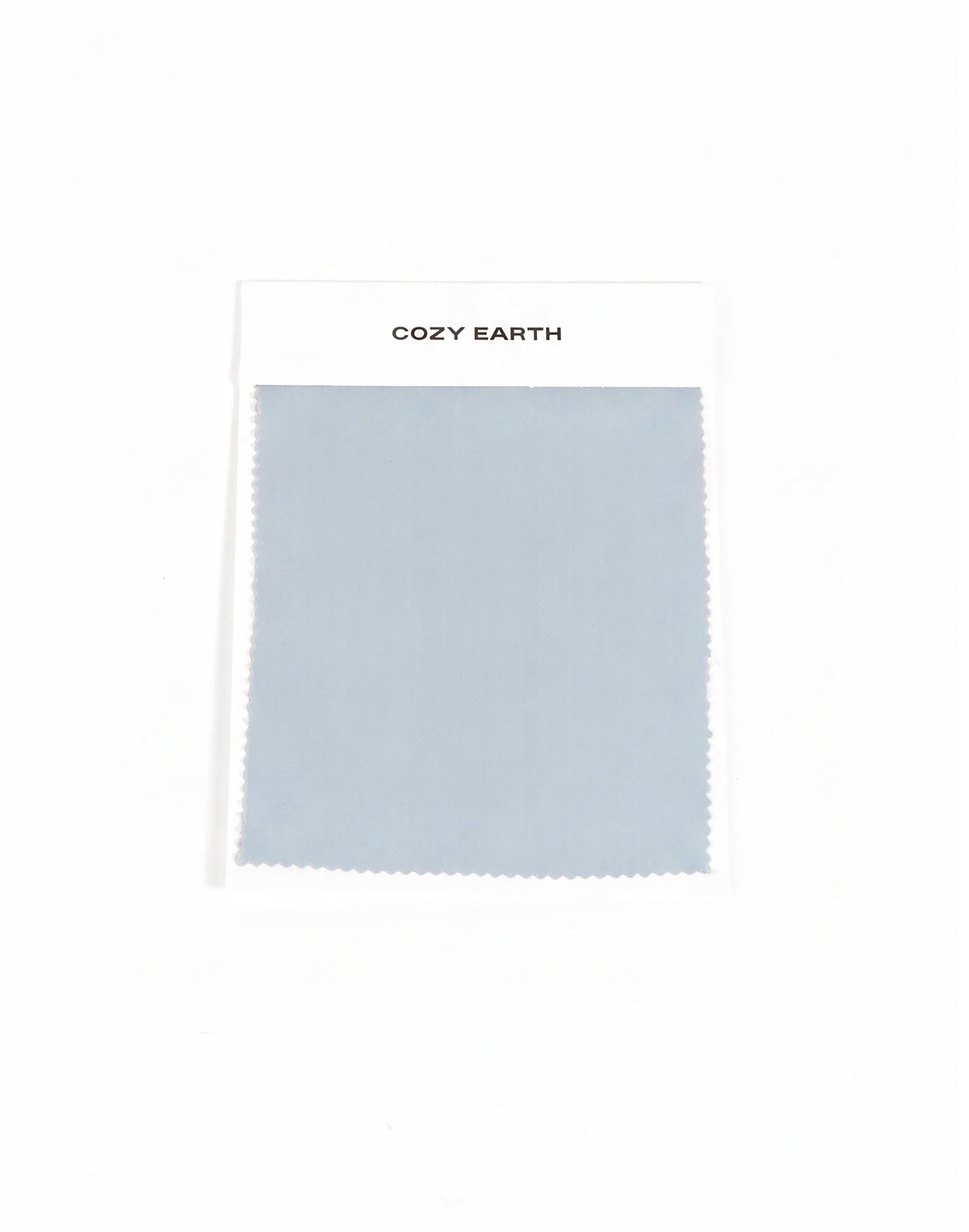 A rectangular light gray-blue Soft-Wash Cotton Sheet Swatch by Cozy Earth is shown on a white card labeled with the brand, set against a plain white background.