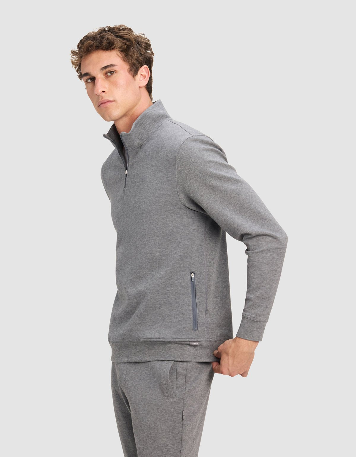 A young man wears the Cozy Earth Men's StretchTech Quarter Zip in light gray with matching sweatpants, standing against a plain background and looking at the camera with a neutral expression.