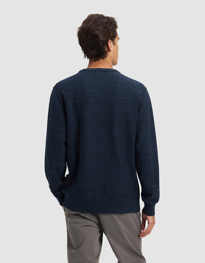 A man stands facing away from the camera, wearing Cozy Earth's Men's Tate Crewneck in dark blue and gray pants against a plain light gray background.