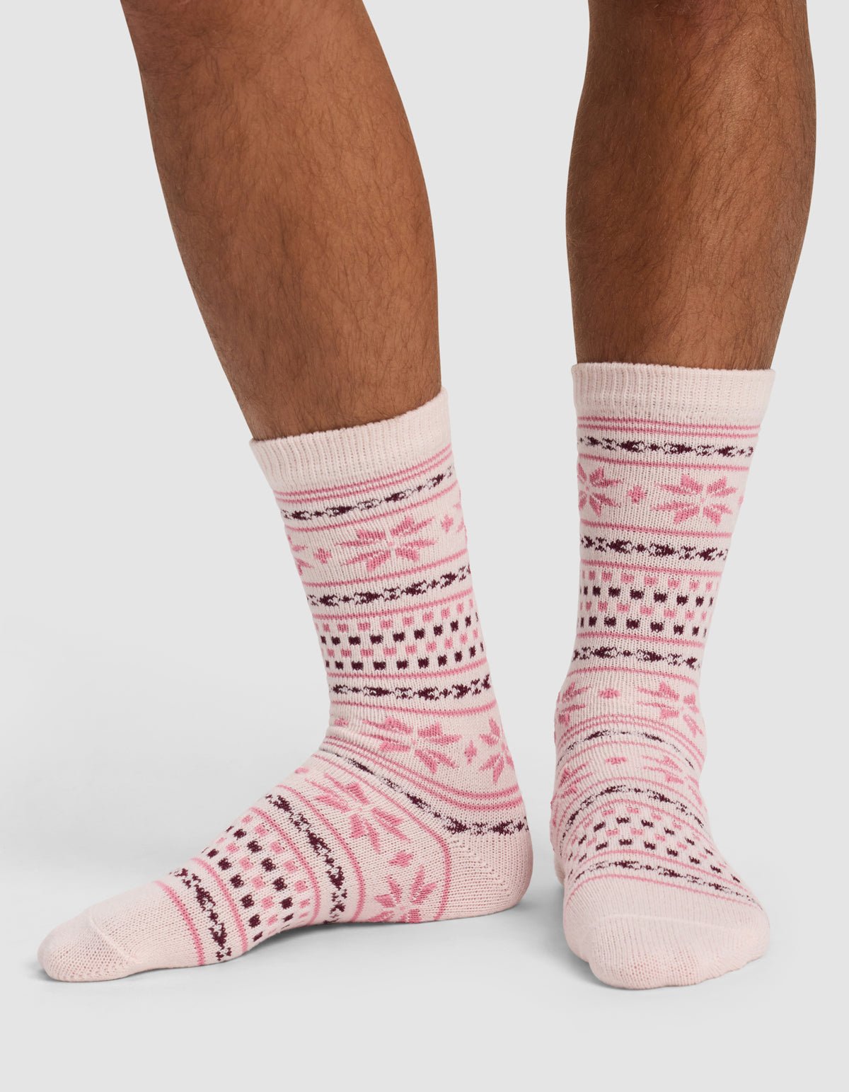 A person wearing Cozy Earth's The Snowflake Plush Lounge Sock in light pink with dark pink and black geometric and floral patterns stands on a white background.
