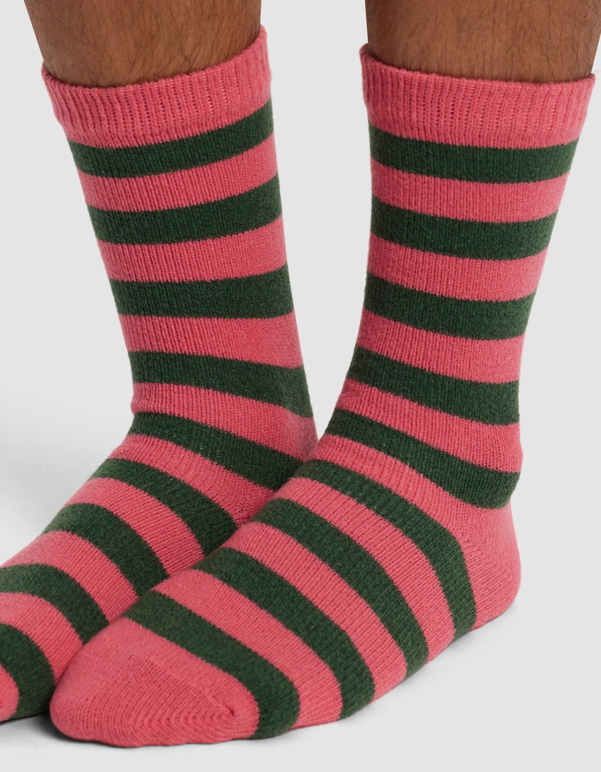 A pair of feet wear Cozy Earth's Striped Plush Lounge Socks, featuring horizontal pink and dark green stripes, against a plain white background.