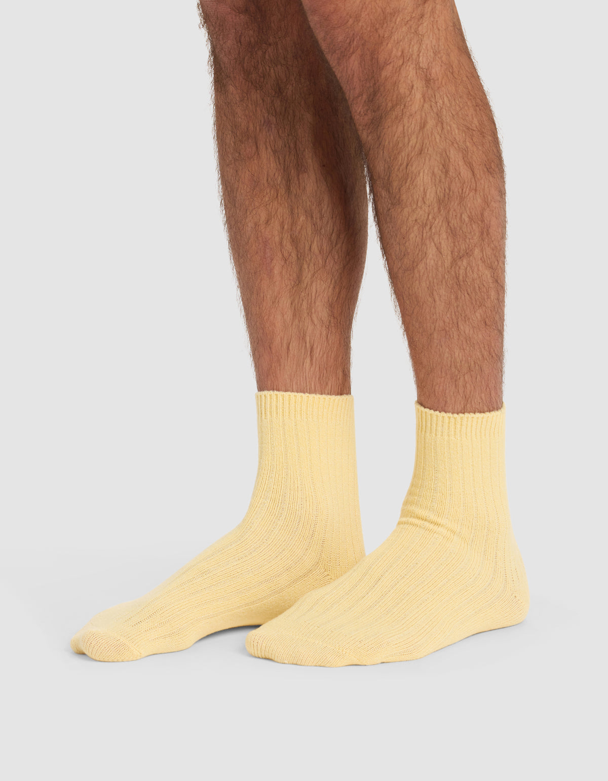 A person with hairy legs is wearing Cozy Earth's Plush Lounge Quarter Socks in light yellow, standing on a plain, light grey background.