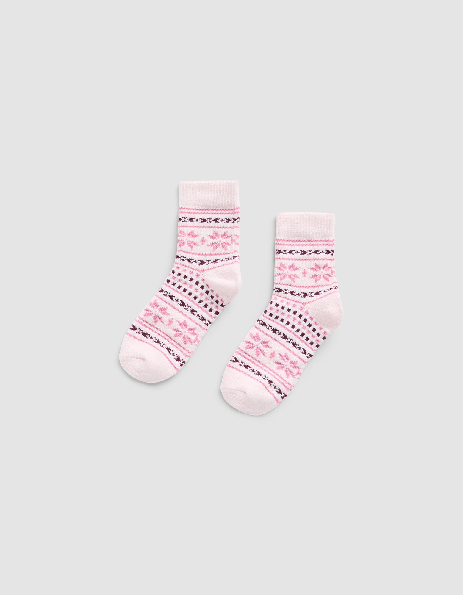 The Snowflake Plush Modern Crew Sock by Cozy Earth is a light pink pair featuring darker pink and black geometric patterns, including stripes and star shapes, displayed flat on a plain gray background.|Color:Ballet