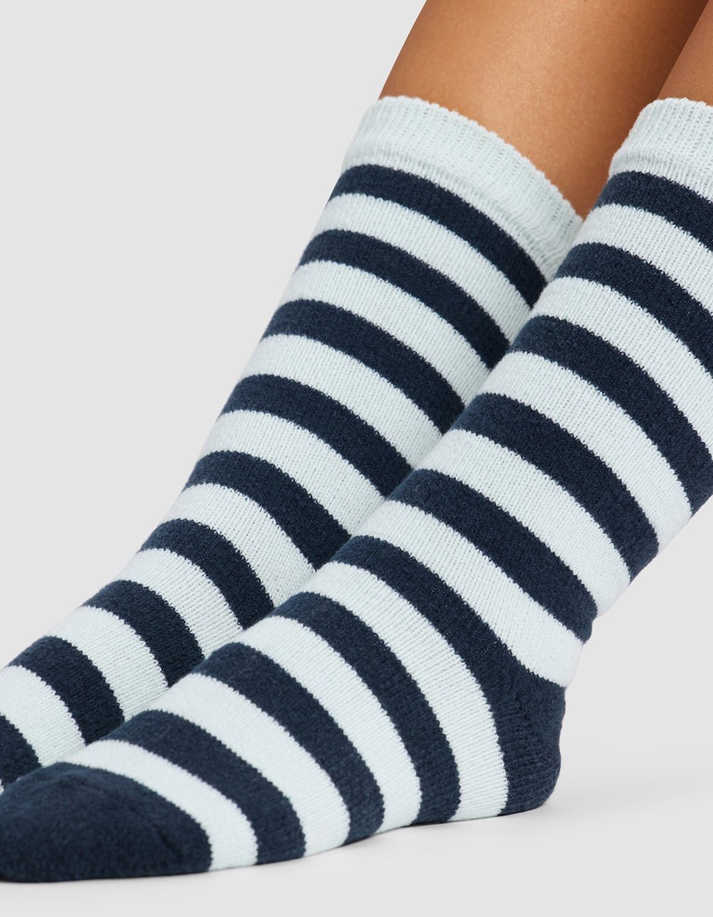 A close-up of two feet wearing Cozy Earth's Striped Plush Lounge Socks, featuring alternating thick black and white stripes, against a plain light background.|Color:Mist Stripe