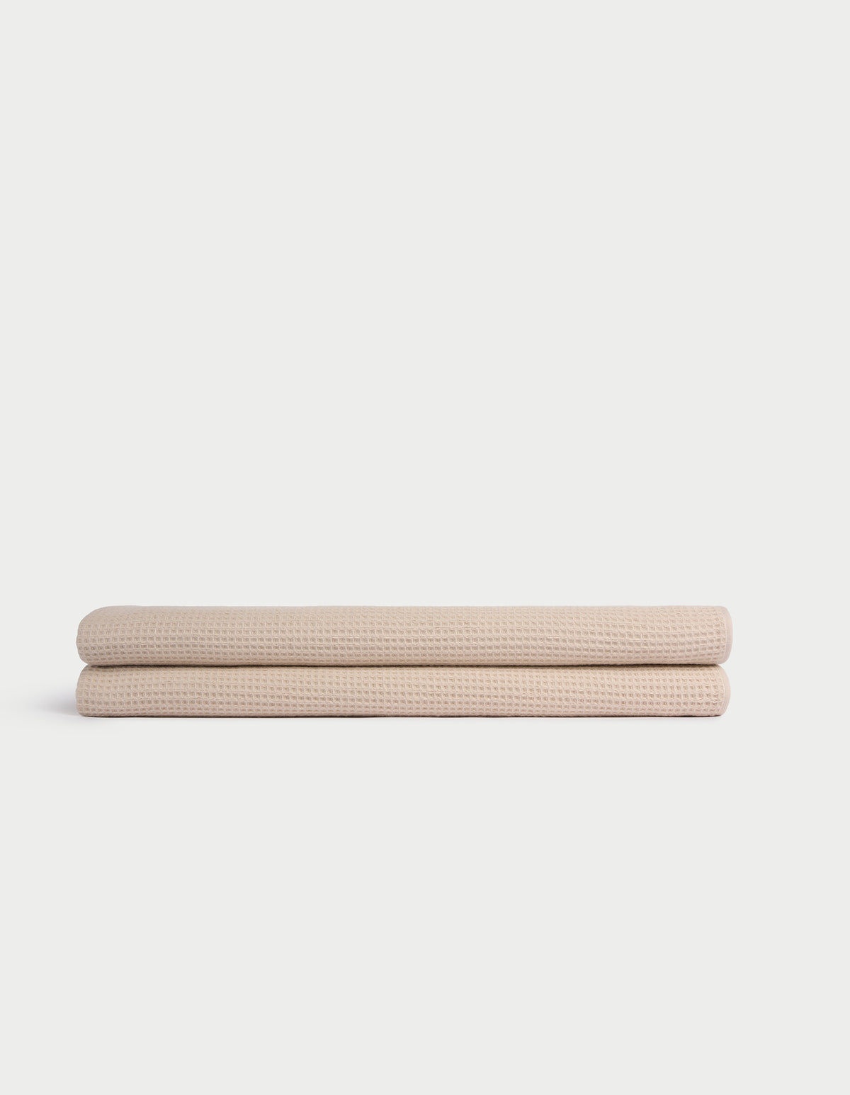 Two Cozy Earth Waffle Bath Sheets, beige and neatly folded, are stacked atop one another against a plain white background. 
