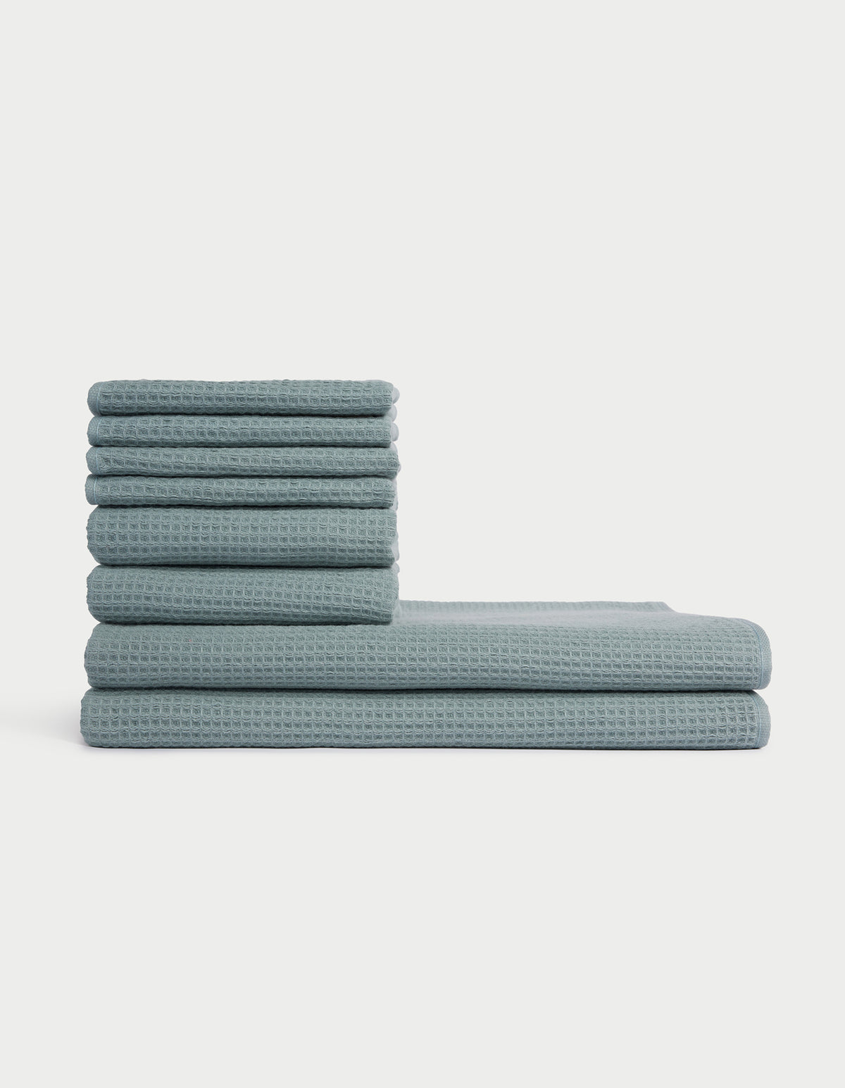 The Cozy Earth Waffle Bath Towel Set features blue, waffle-textured towels stacked in two vertical piles of varying heights against a plain white background. |Color:Brook