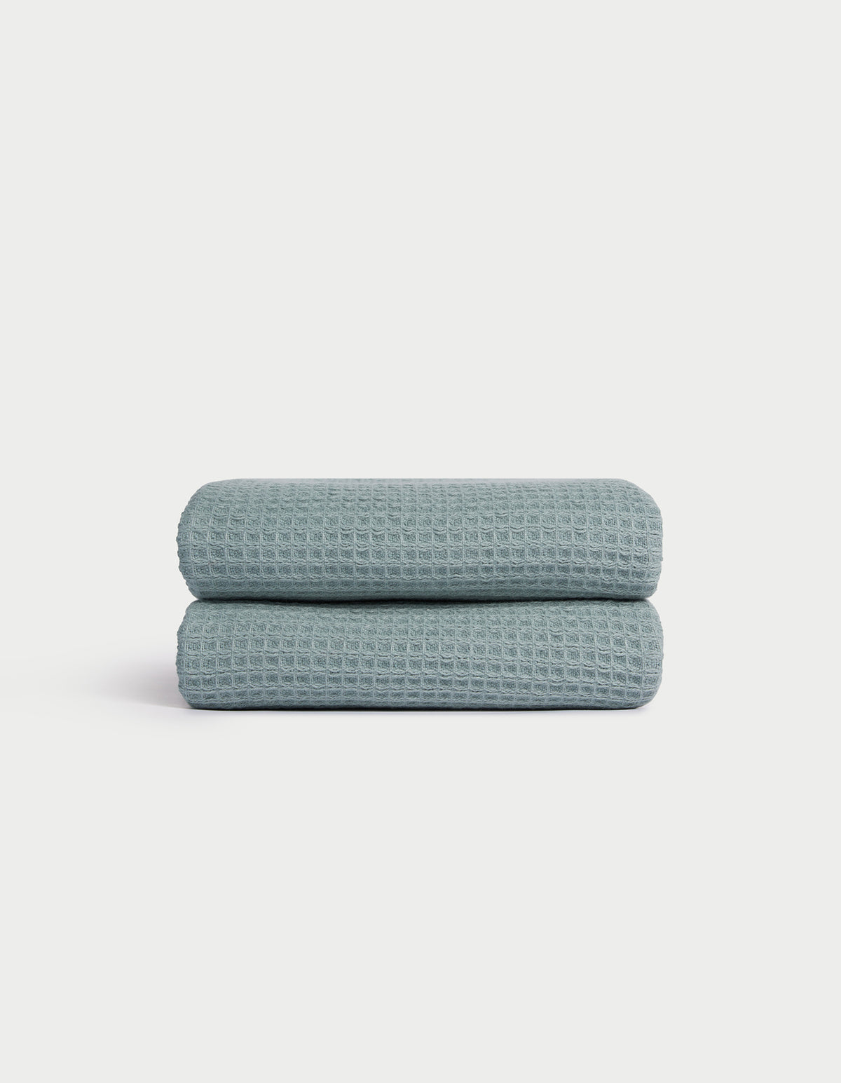 A folded Cozy Earth Waffle Hand Towel in light blue with a textured waffle pattern is displayed on a white background. 