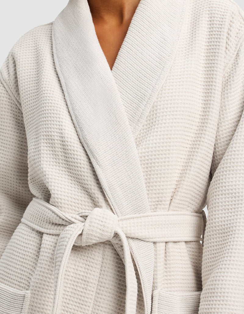 A person wears the Cozy Earth Waffle Bath Robe in light beige, featuring waffle texture, wide lapels, two front pockets, and a matching waist tie.