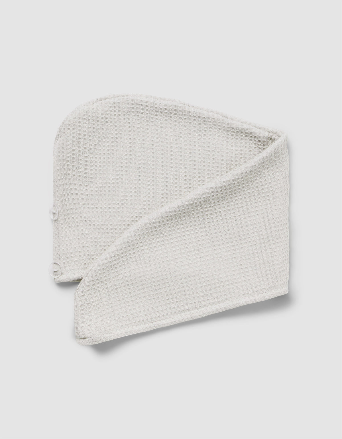 The Cozy Earth Waffle Hair Towel, a folded, textured white headband with snap buttons at one end, is displayed on a light gray background.