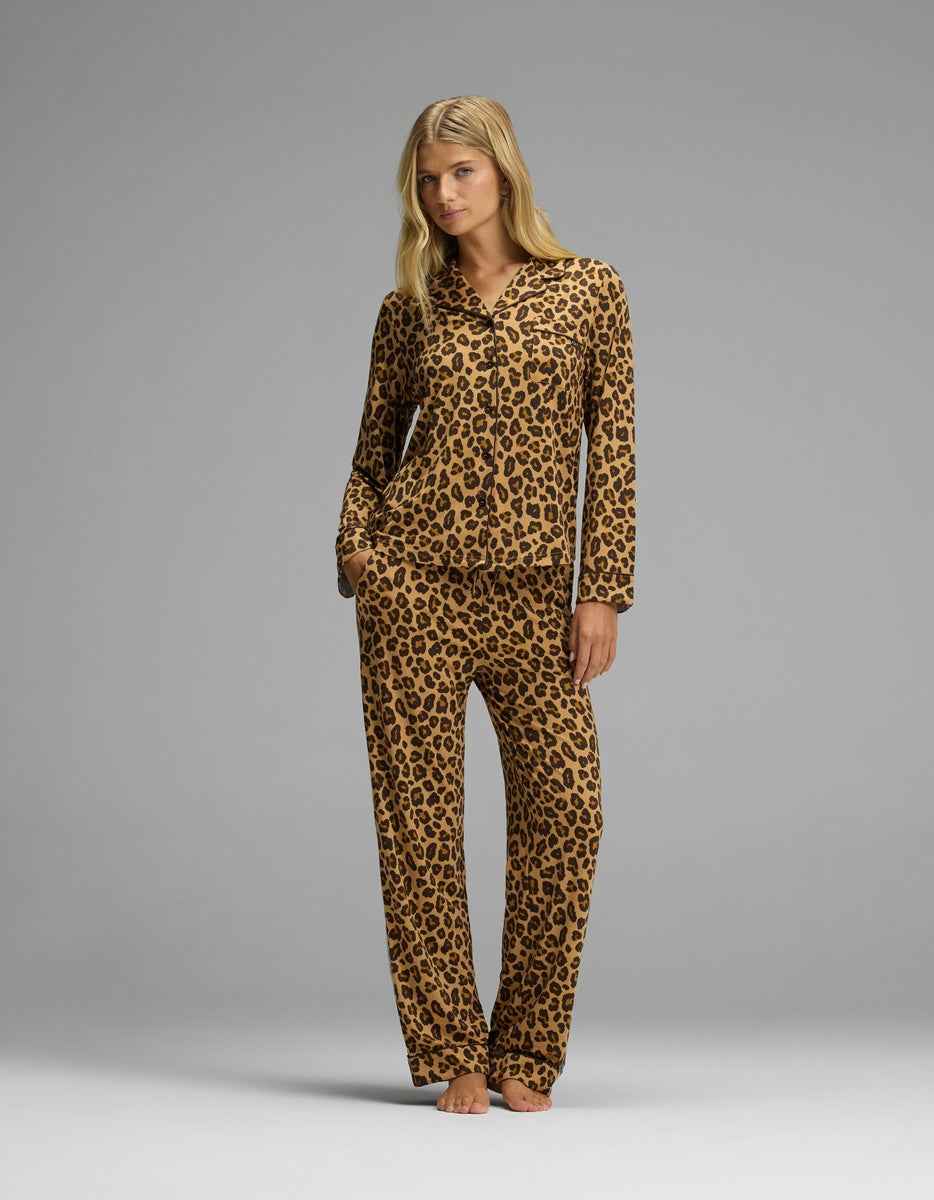 A woman wearing a brown and black leopard print Women’s Bamboo Stretch-Knit Long Sleeve Pajama Set consisting of a long-sleeved button-up top and matching pants.