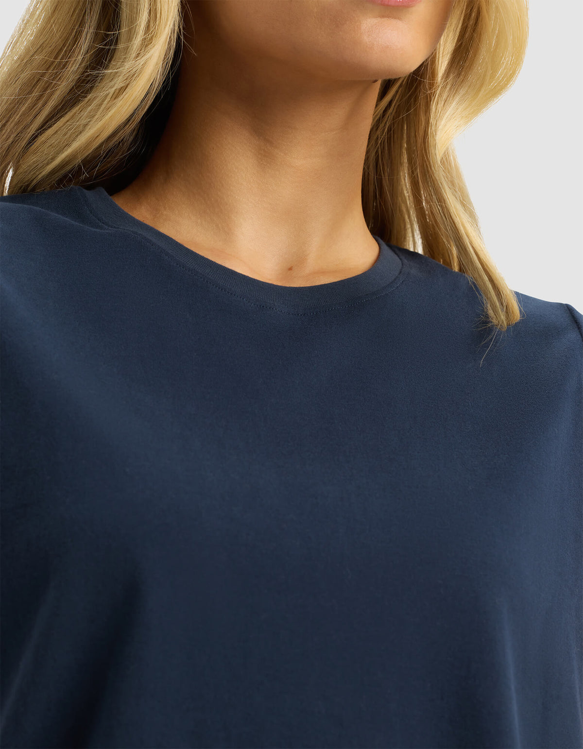 Close-up of a woman wearing the Cozy Earth Women's All Day Sleeveless Tee in navy blue, showing her neck, collar, and part of her blonde hair against a neutral light gray background.
