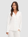 A woman smiles against a light gray background wearing HIDE's Women's Bamboo Stretch-Knit Long Sleeve Pajama Top with matching pants. |Color:Ivory