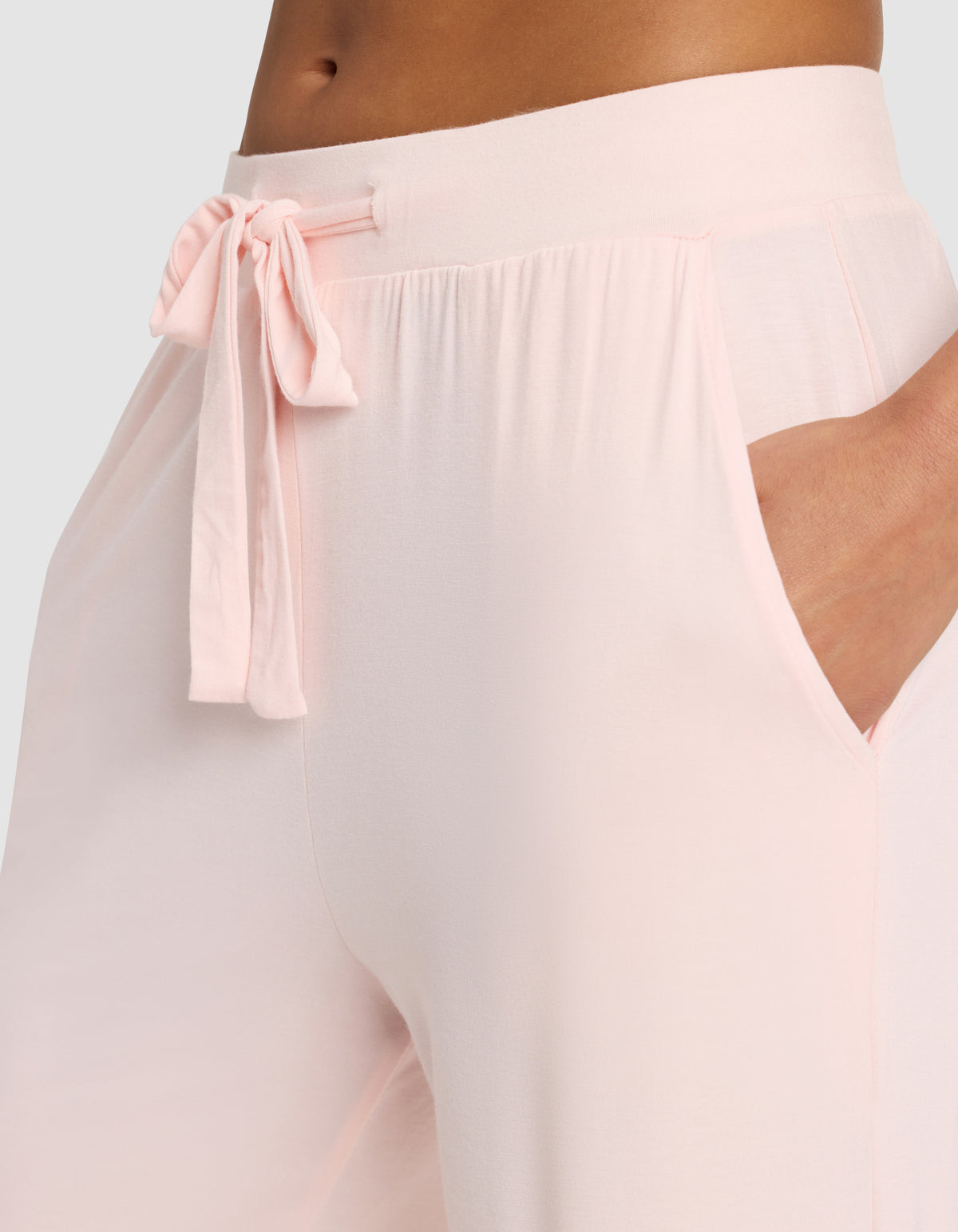 A woman wears Cozy Earth's Women's Bamboo Stretch-Knit Pant in light pink, featuring a drawstring bow at the waist and her hand in the side pocket.