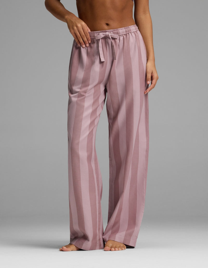 A person stands barefoot wearing Cozy Earth’s Women’s Belmont Pajama Pant, featuring a loose fit, pink color, vertical stripes, and a drawstring waist. The upper body is mostly out of frame.