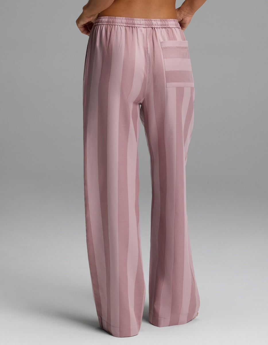 A woman is shown from behind against a plain gray background, wearing Cozy Earth’s Women’s Belmont Pajama Pant—loose, high-waisted pink pants with vertical stripes and a back pocket.|Color:Viola Stripe