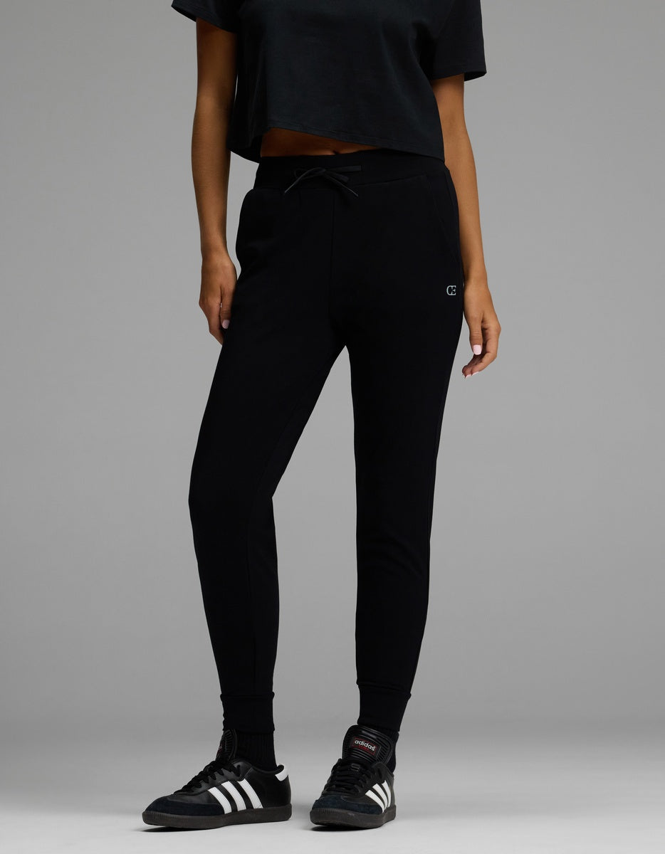 A person wearing the Cozy Earth Women’s Brushed Bamboo Jogger in black, along with a black cropped t-shirt and black Adidas sneakers, stands against a plain gray background. Their face is not visible.