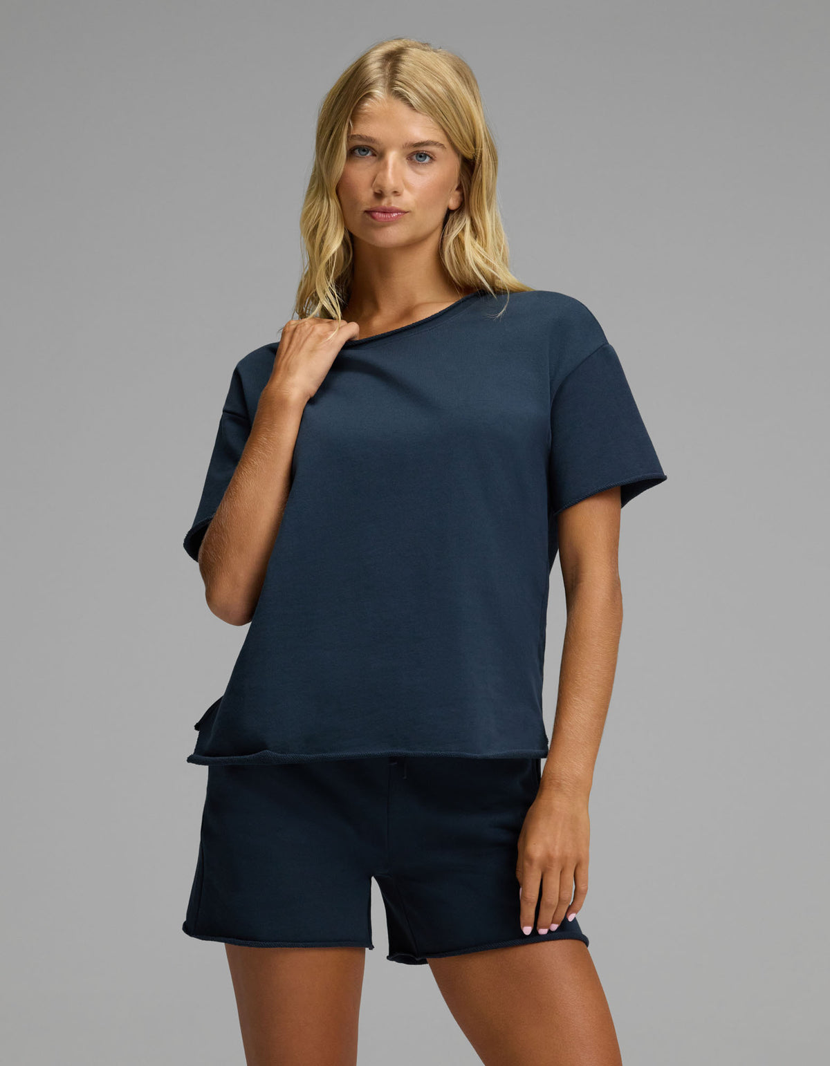 A woman with blonde hair wears the Cozy Earth Women’s Chelsea Short Sleeve Set in Eclipse, standing against a plain gray background and looking at the camera with a relaxed expression.