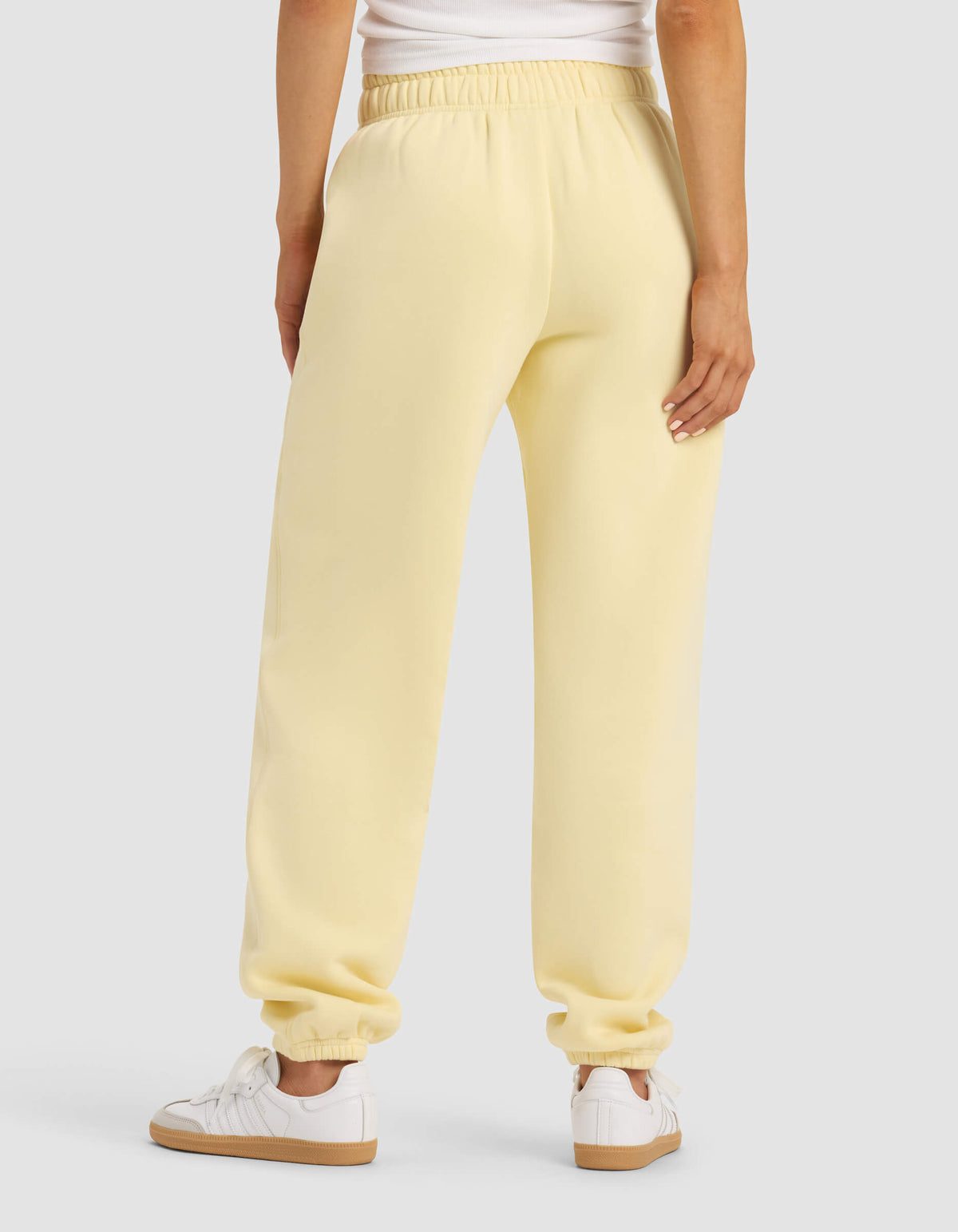 A woman is shown from the back wearing Cozy Earth’s Women's Cityscape Sweatpant in light yellow, paired with a white top and white sneakers, standing against a plain light gray background.