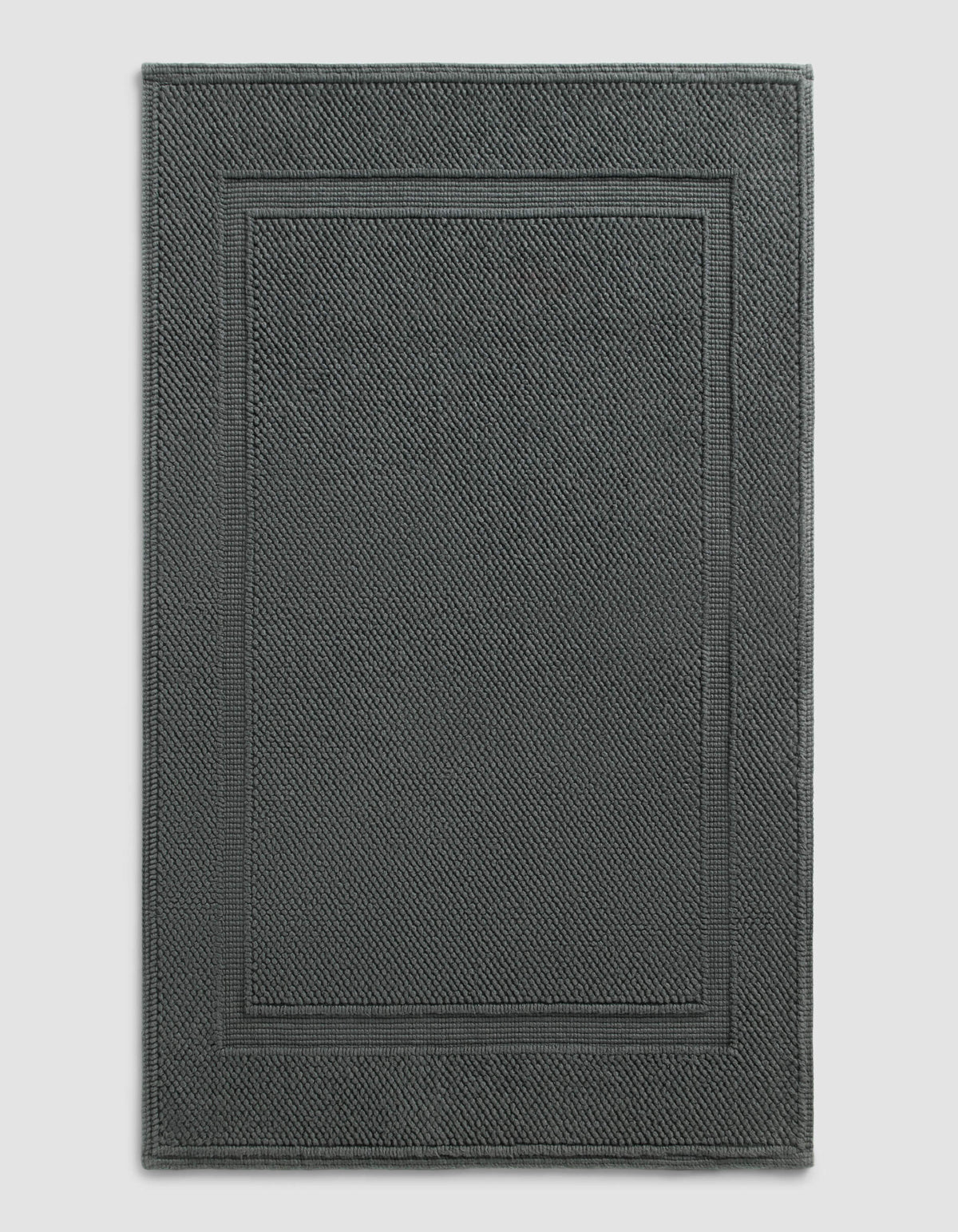 The Cozy Earth Classic Bath Mat features a dark gray, rectangular design with a textured surface and double border, shown against a plain light background.