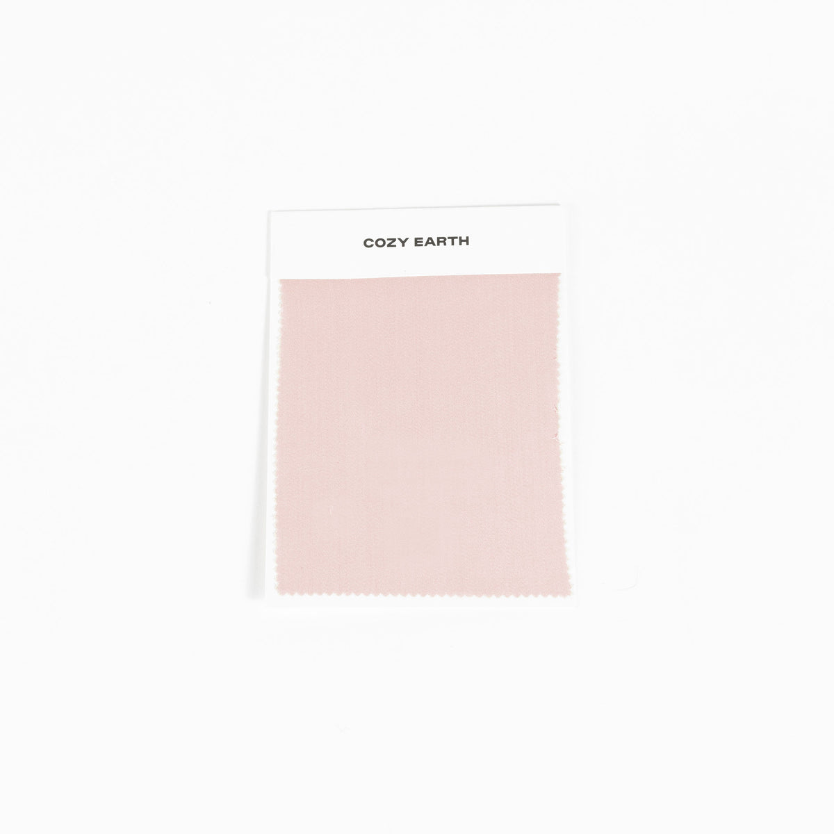 A sample swatch of Bamboo Sheet fabric from Cozy Earth, in light pink, is displayed on a white card against a white background.