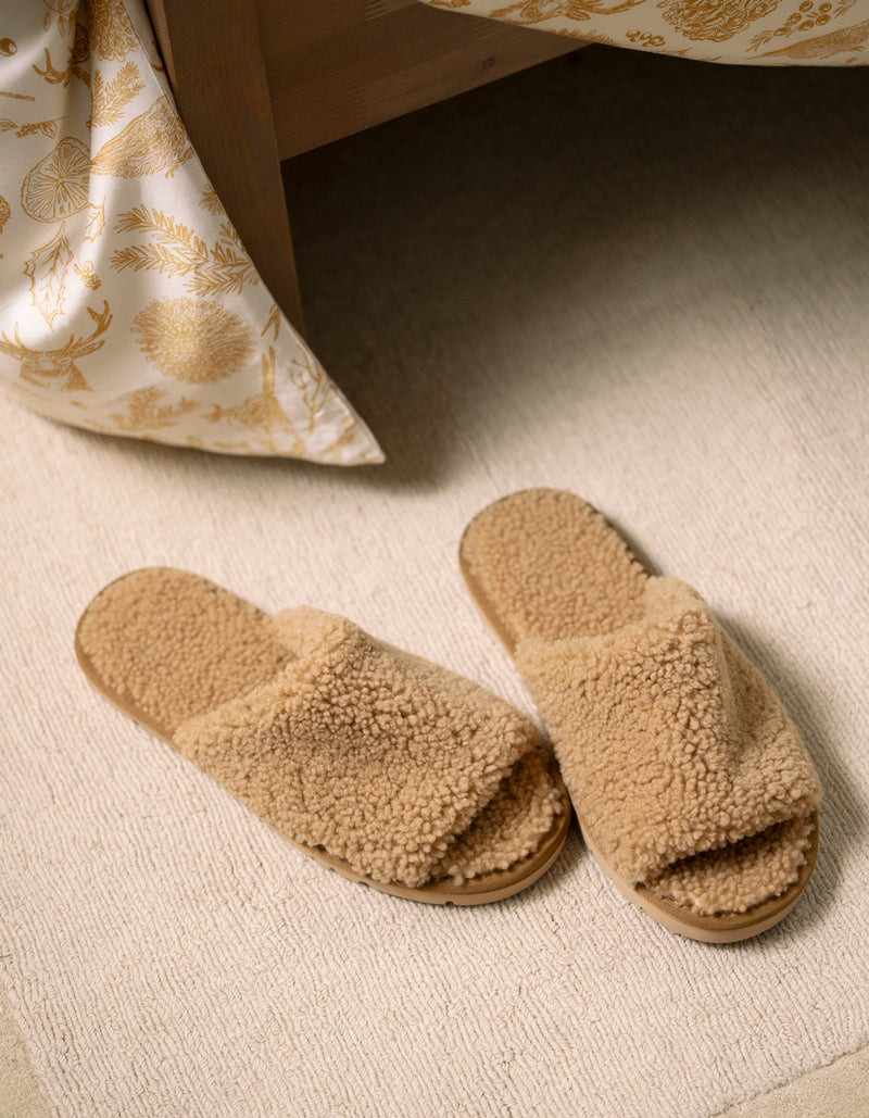 Pair of beige Cozy Earth Puffy Sheep Slides on a carpeted floor