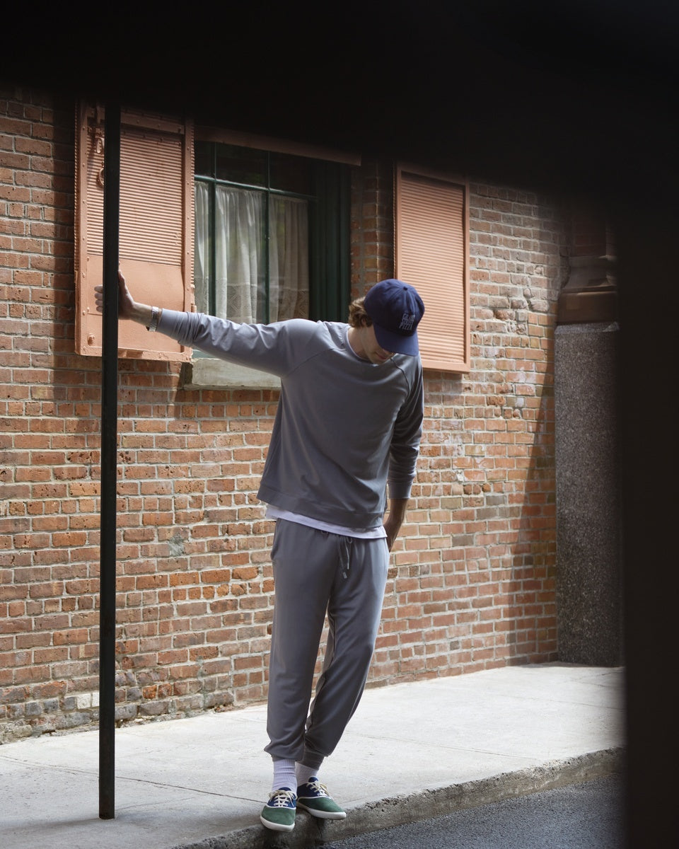Man in a grey sweatshirt and matching joggers in a brick alleyway