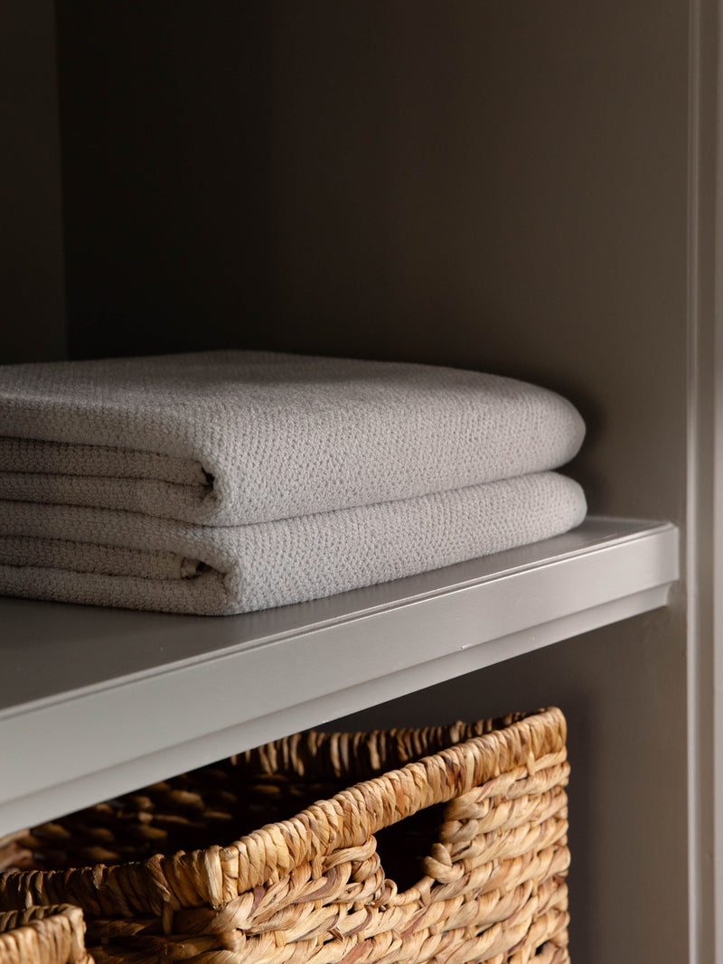 Nantucket Bath Towels in the color Heathered Light Grey. Photo of Nantucket Bath Towels taken as the towels rest on a shelf in a bathroom.