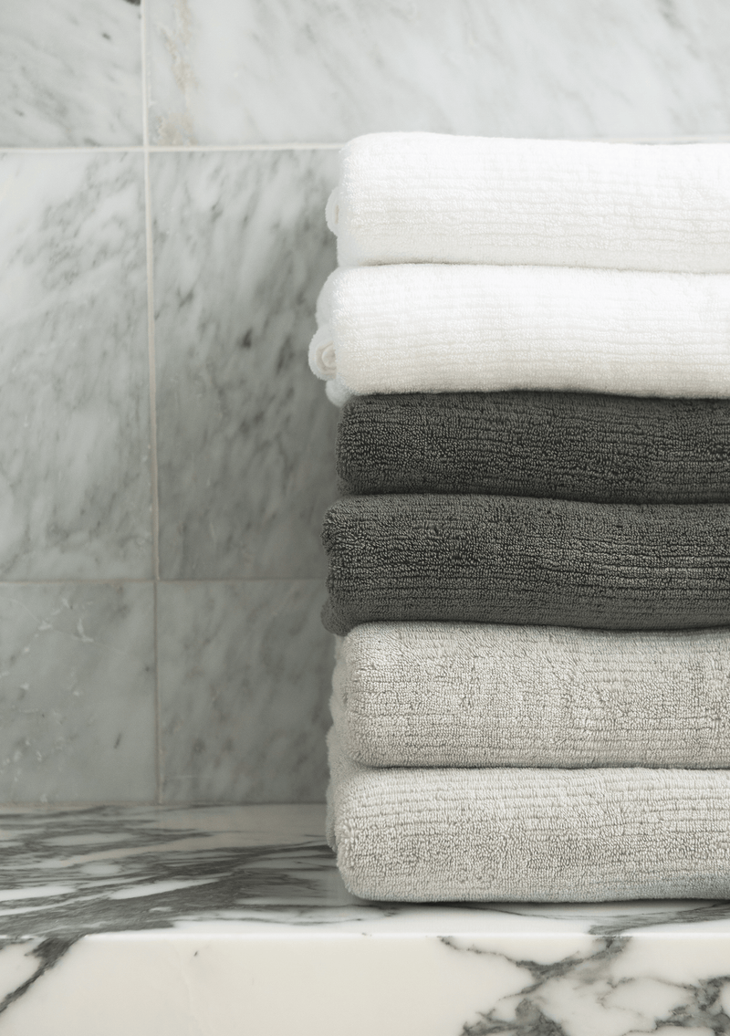 Ribbed Terry Hand Towel in the colors Light Grey, Charcoal, and White. Photo of Ribbed Terry Hand Towel taken with the Ribbed Terry Hand Towel resting on a bathroom sink.